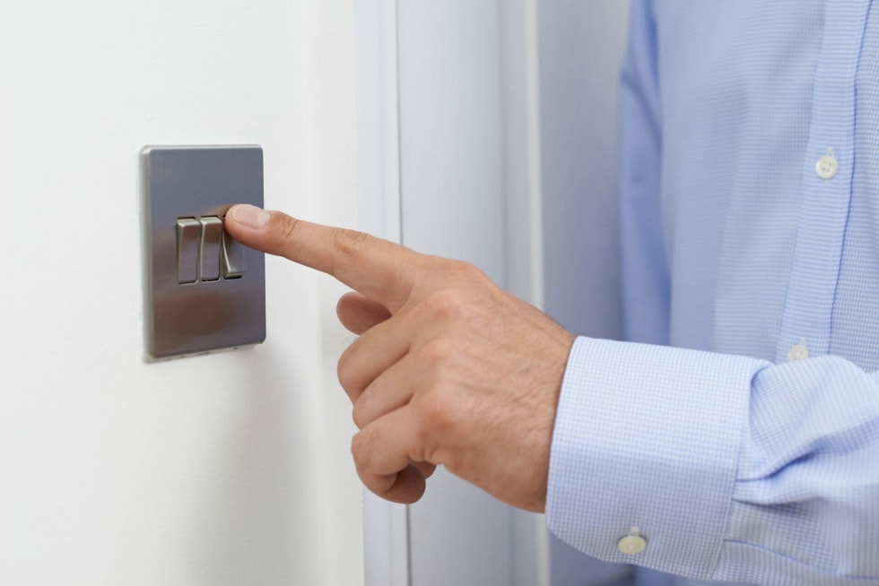 A mans hand pressing a traditional satin stainless light switch