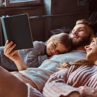 Parents and their little girl lying back cuddling and reading a book
